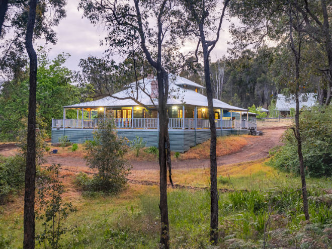 Stone's Throw Cottage in Bridgetown, lights on the wrap-around veranda, as seen from amongst the surrounding trees.