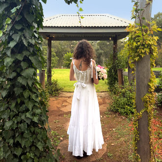 A bride in her wedding dress, holding a flower bouquet, stands in the Black Cockatoo Cellar Door garden, looking out to the lawn and forest trees.