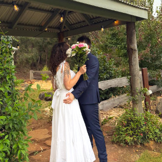 A wedding couple make a secret kiss behind a flower bouquet in the Black Cockatoo Distillery Cellar Door garden.